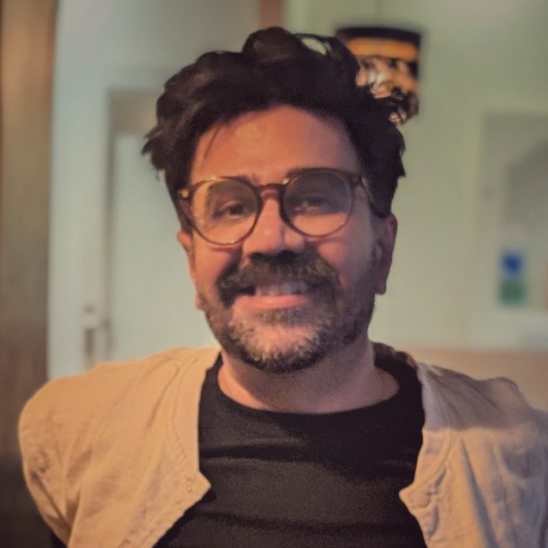 Rohan Mann, smiling, in glasses and an open cream shirt